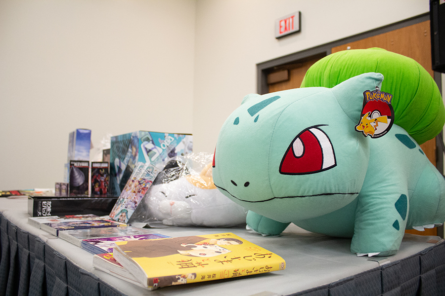 A giant Bulbasaur plush among other books and model kits on a table.